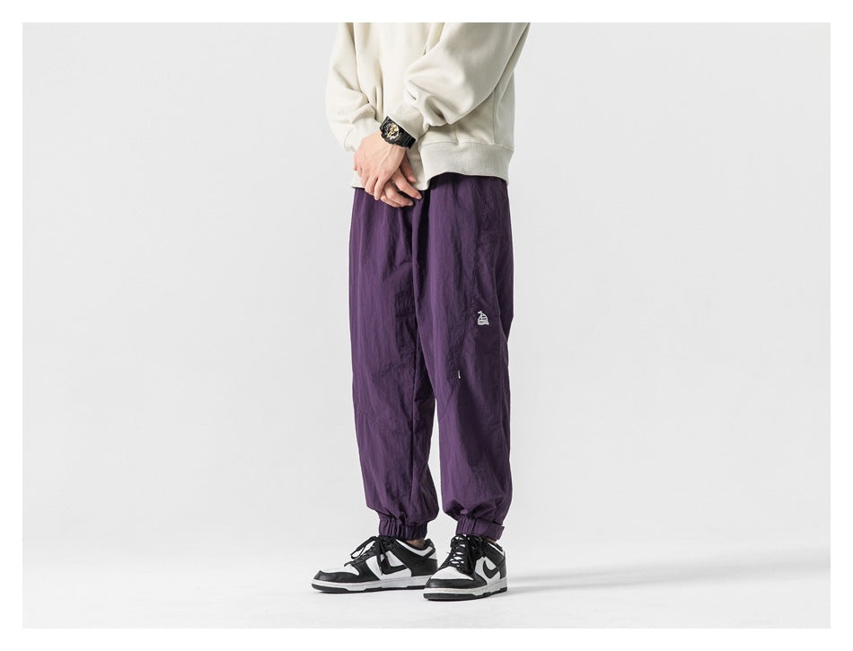 Model wearing purple loose-fit jogger pants with elastic cuffs, shown from the front at an angle.