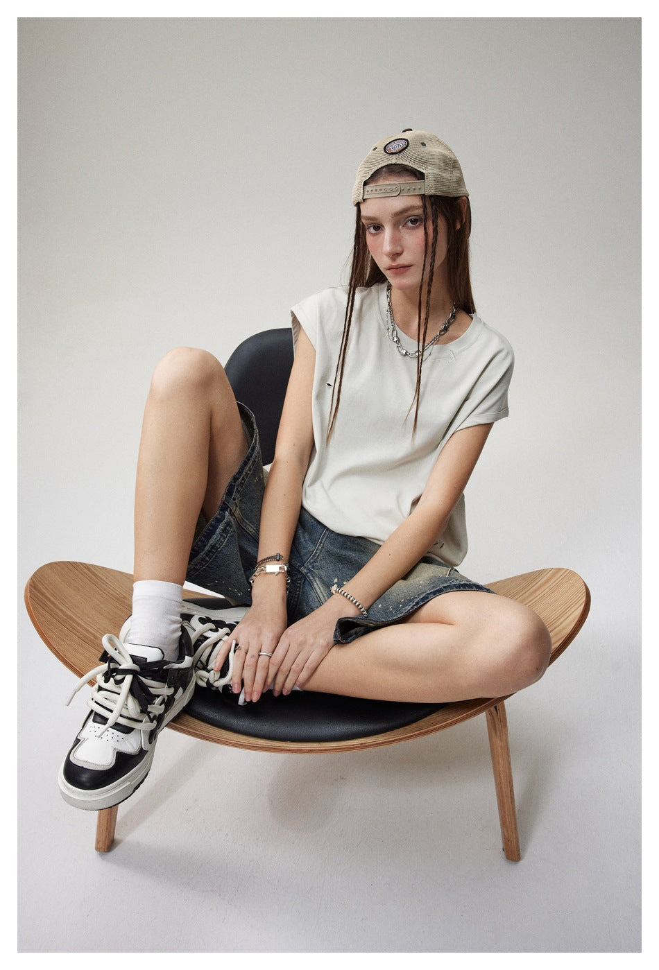 Seated model wearing a loose white cap-sleeve T-shirt with small distressed slits, shown from the front.