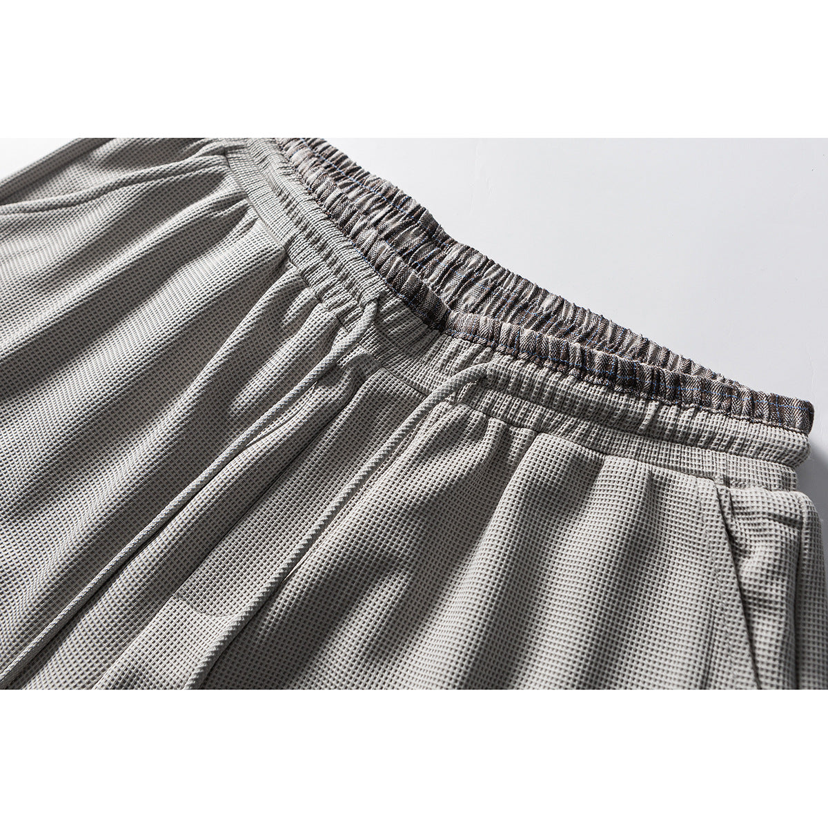 Close-up of light gray textured trousers showing the gathered elastic waistband and stitching.
