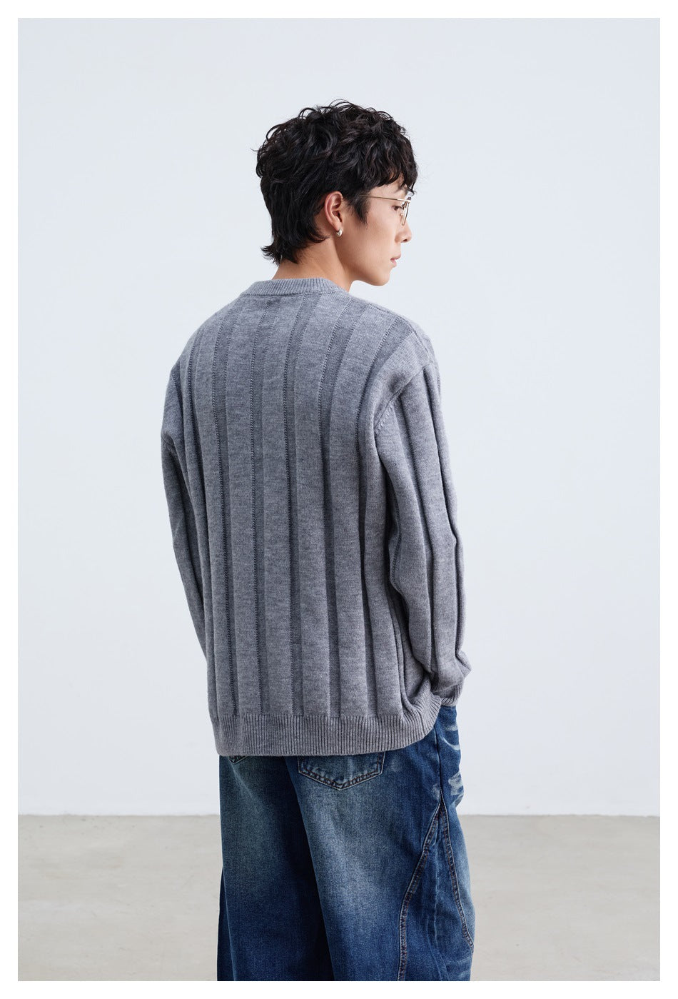 Rear view of a model wearing a gray sweater with vertical panels and a ribbed hem.