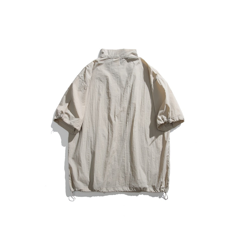 Beige short-sleeve jacket laid flat from the back, with a high collar, gathered sleeve ends, and drawcord hem.