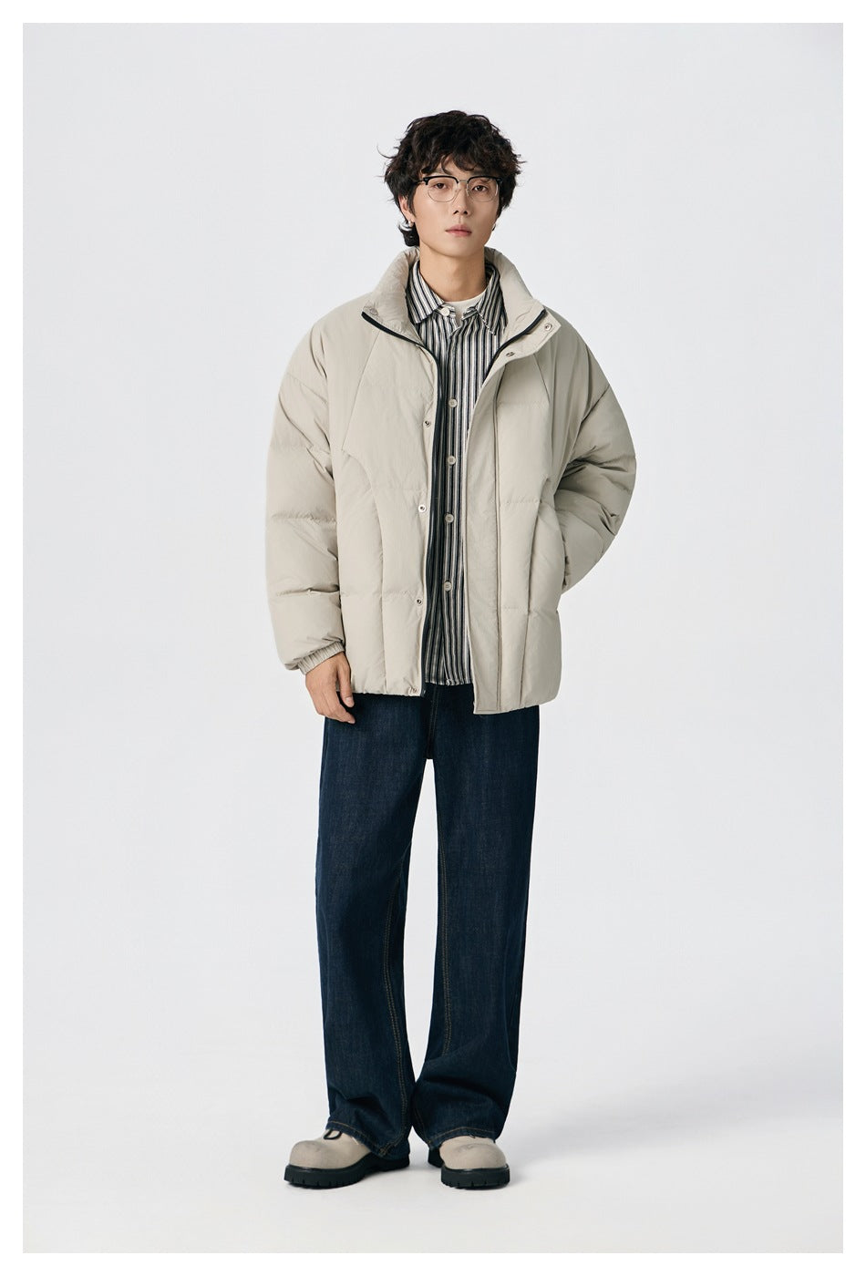 Front view of a model wearing a light beige padded jacket over a striped shirt with dark wide-leg jeans.