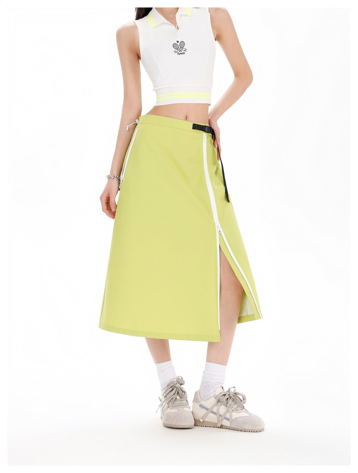 Model wearing a white sleeveless tennis top and lime-green midi skirt with a white zippered side slit and black belt detail.