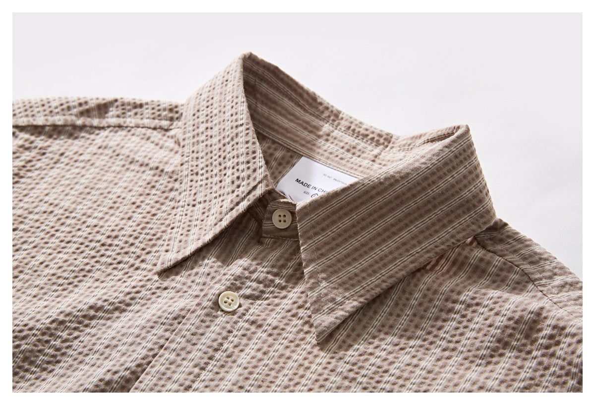Close-up of a beige-brown patterned shirt collar, button, and neck label.