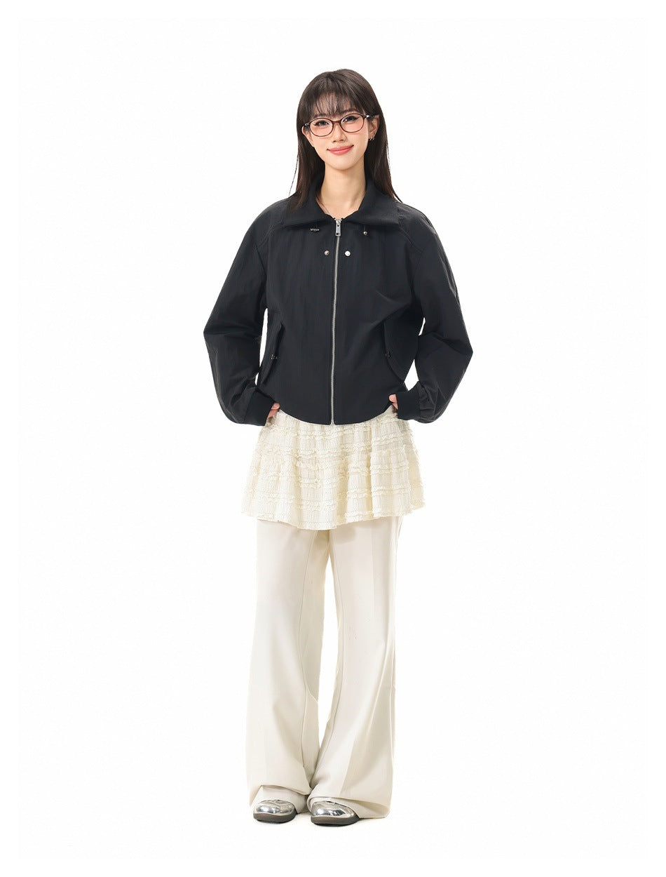 Front view of a model wearing a black collared zip jacket with flap pockets over a cream lace top and trousers.