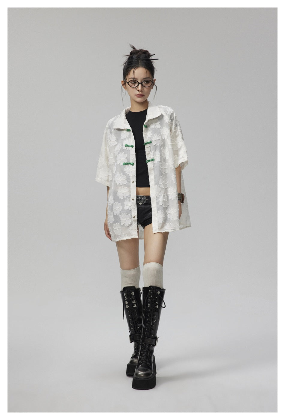 Model wearing a white short-sleeved floral shirt with green frog closures, black top, and shorts.