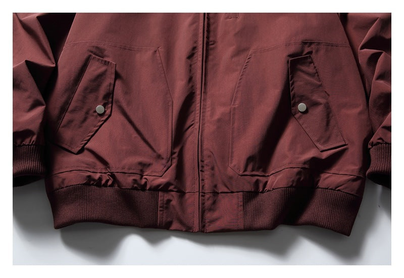 Cropped front view of a burgundy jacket with two flap pockets, a center zipper, and ribbed cuffs and hem.