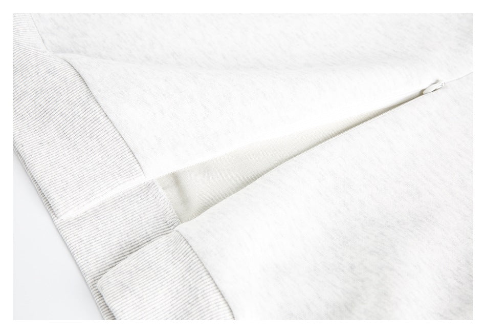 Close-up of a zipper opening on a light heather gray garment beside ribbed trim.
