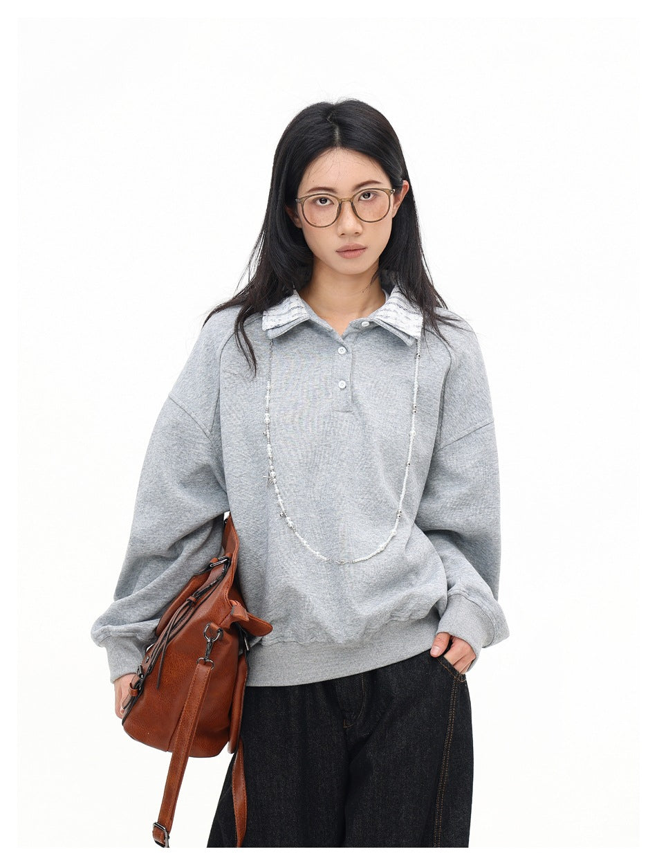 Model in a heather gray collared sweatshirt with a brown shoulder bag, beaded necklace and dark jeans