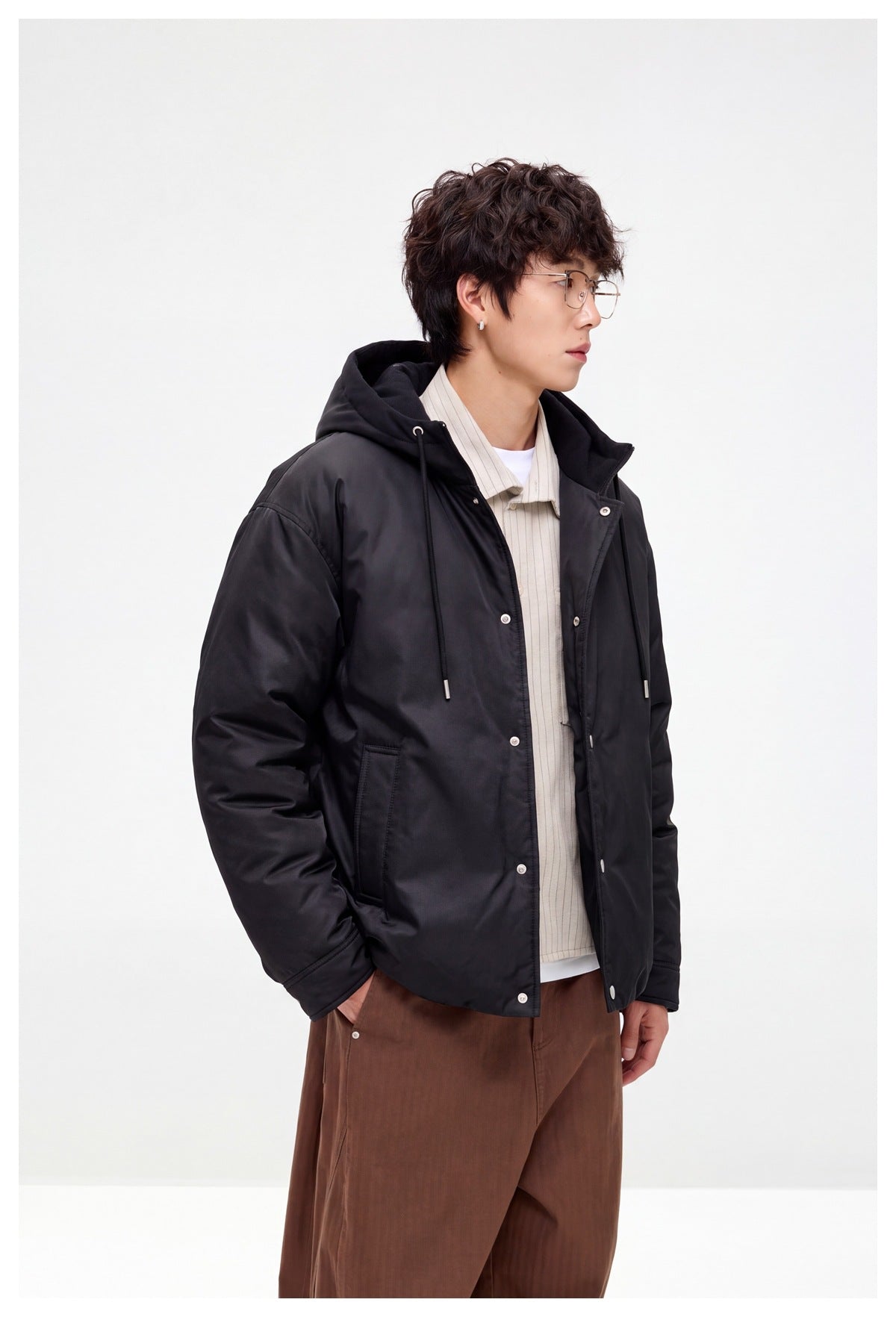 Side view of a model wearing a black hooded jacket with snap closure and front pockets.