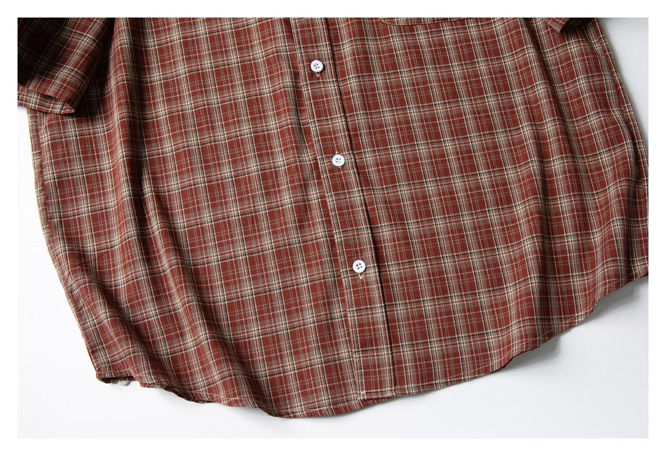 Flat-lay view of the rust-red plaid shirt front, with white buttons and a curved hem.