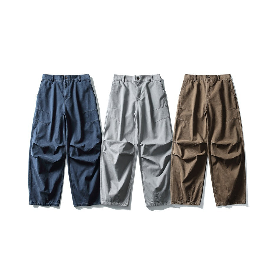 Three pairs of loose trousers shown from the front in navy, light gray and brown, with roomy legs and knee panels.