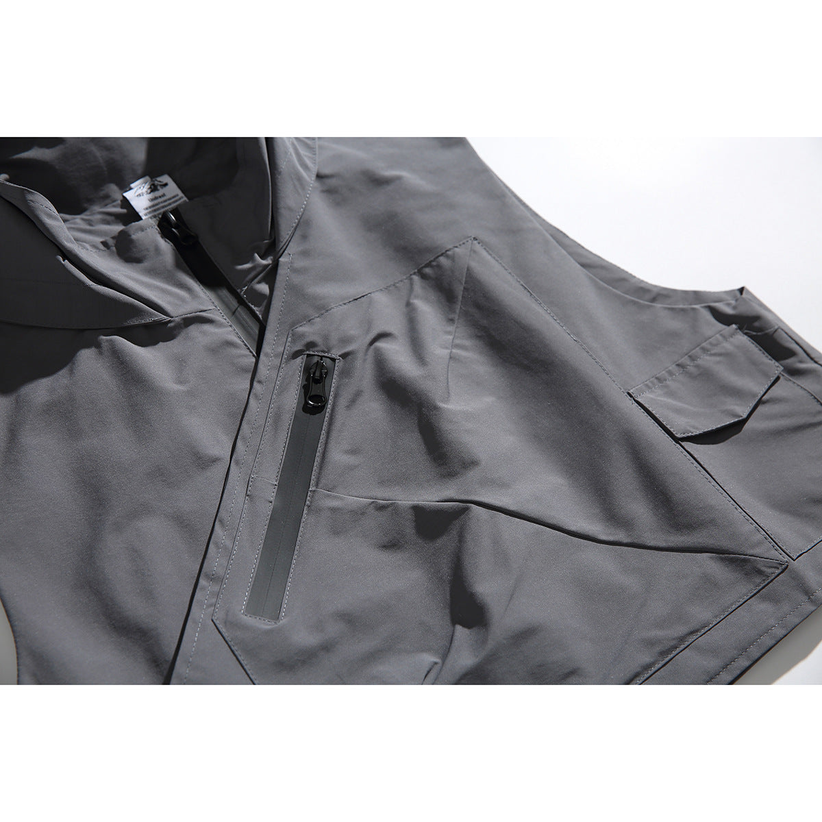 Close-up of a gray vest showing its black vertical zipper pocket and angular flap pockets.