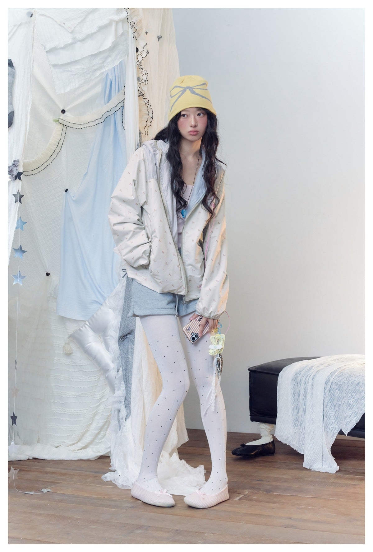 Full-length model wearing an off-white tiny-print hooded jacket, gray shorts, dotted white tights, and a yellow beanie.