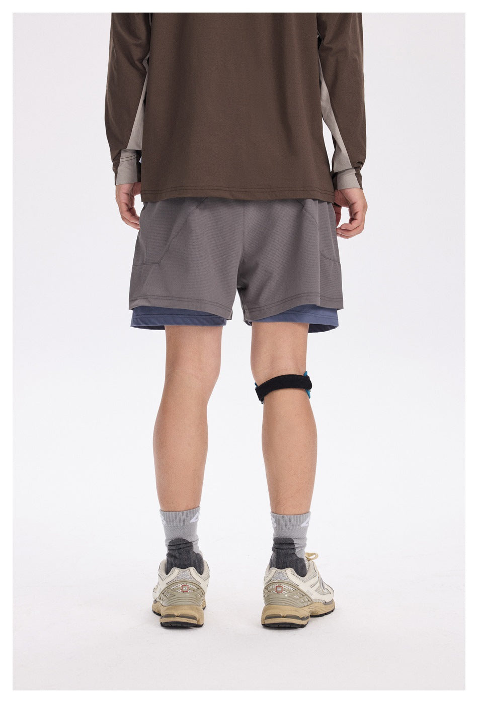 Rear view of a model wearing gray running shorts over blue-gray compression shorts.