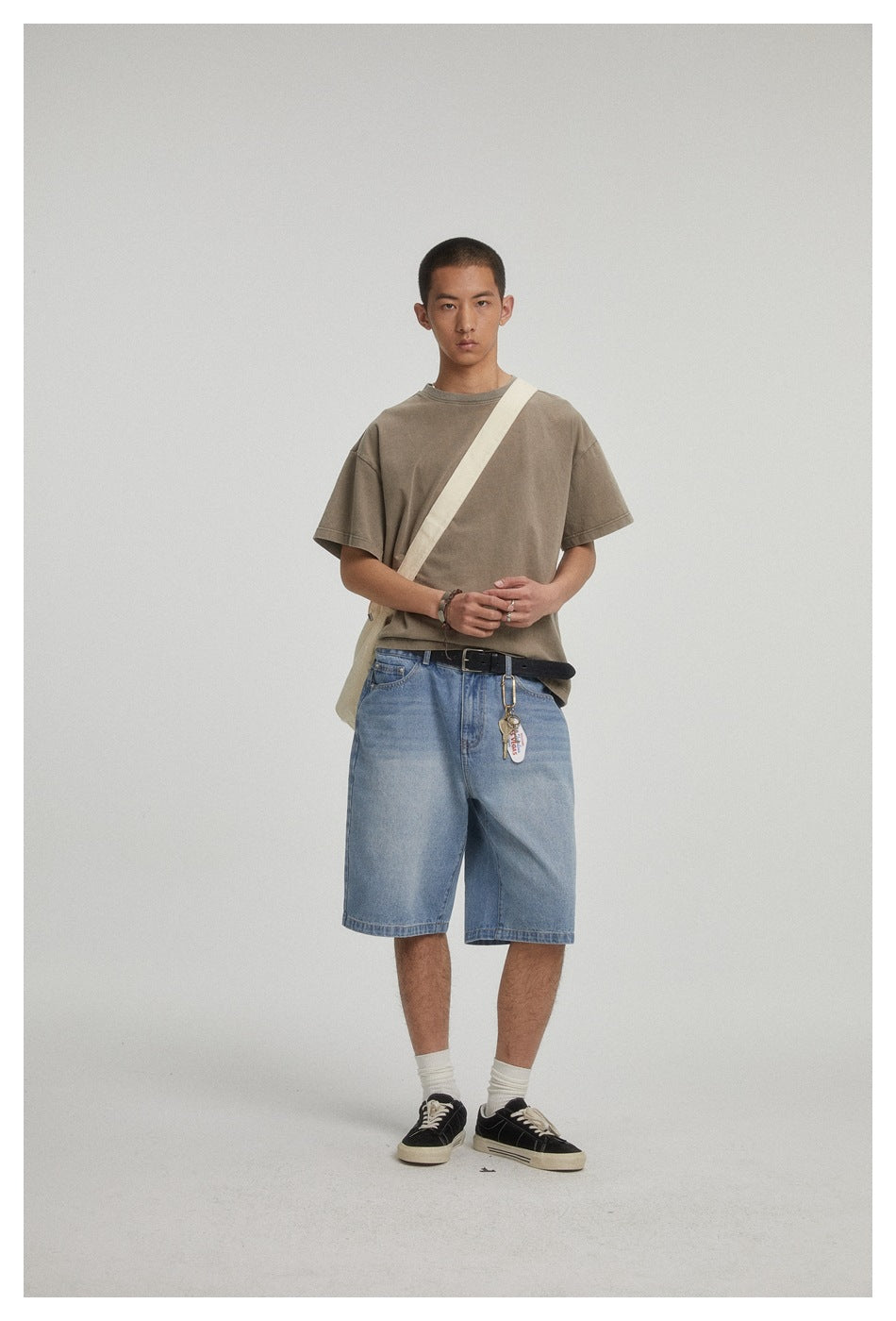 Model wearing a taupe oversized T-shirt, light blue denim shorts, and a cream crossbody strap.