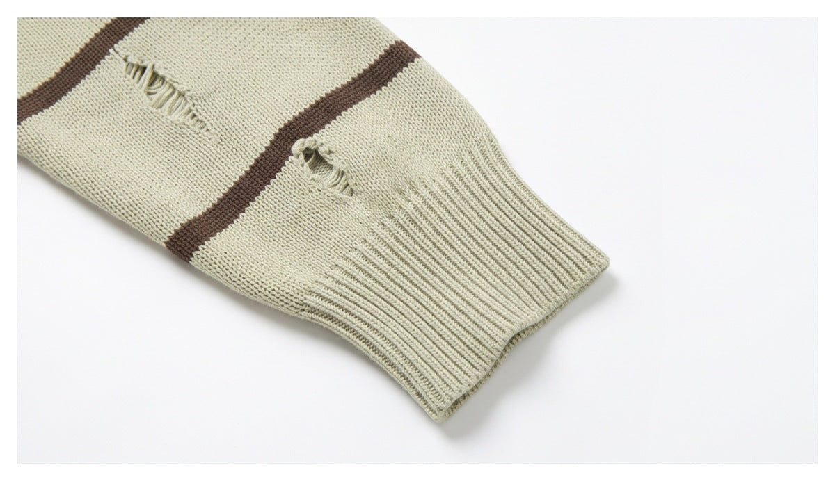 Close-up of a pale beige sweater sleeve with brown stripes, distressed holes, and a ribbed cuff.