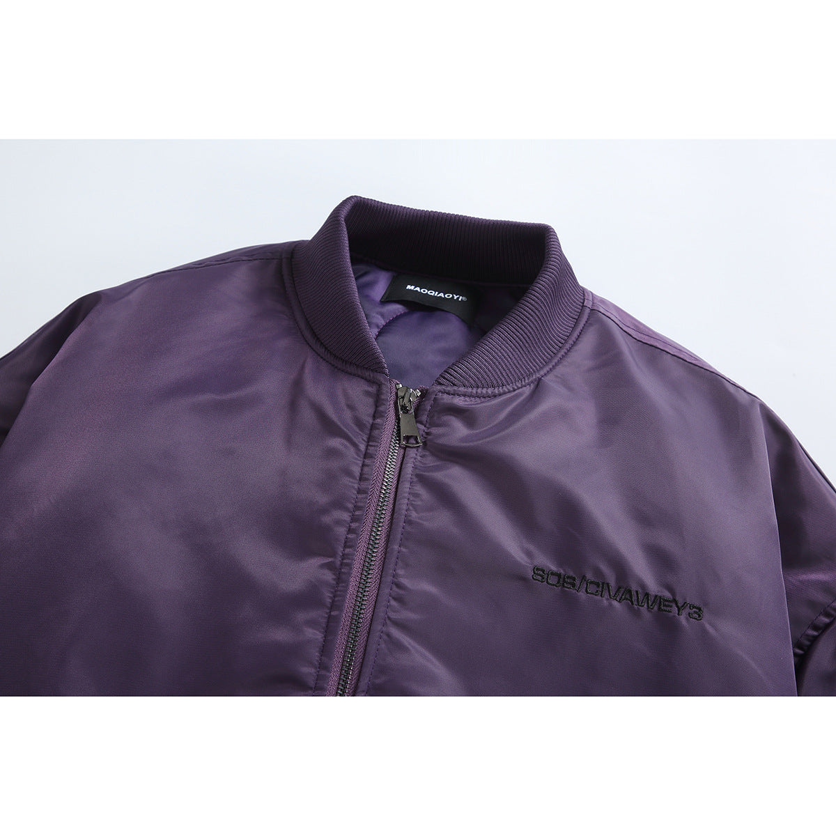 Close-up of a purple bomber jacket collar, zipper, inner neck label and small black chest embroidery.
