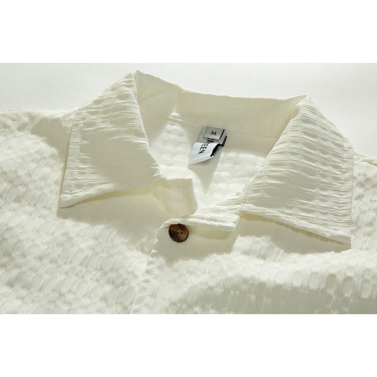 Close-up of an ivory short-sleeve shirt collar, brown button, and textured fabric.