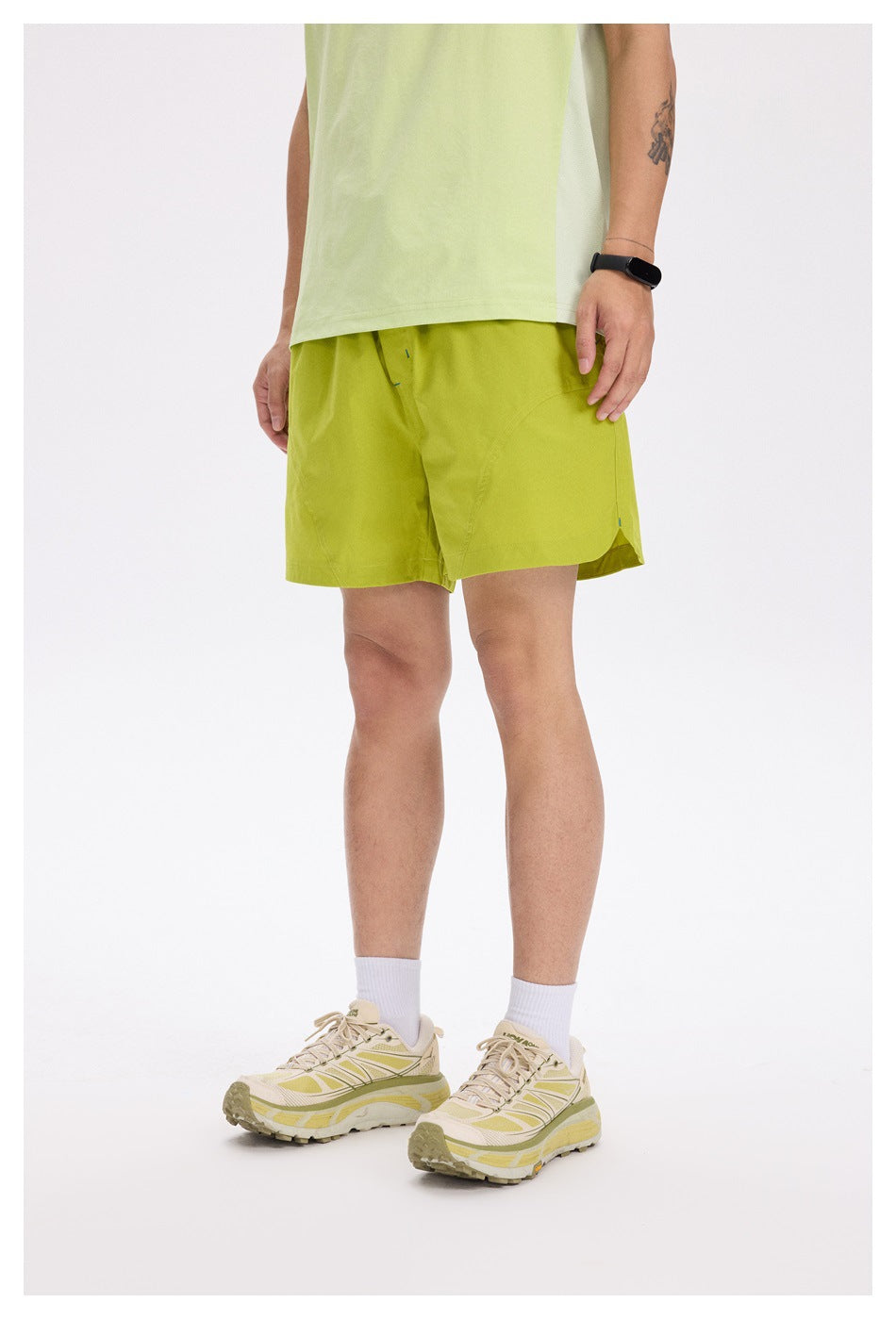 Model wearing yellow-green shorts with a light green top and cream sneakers, front three-quarter view