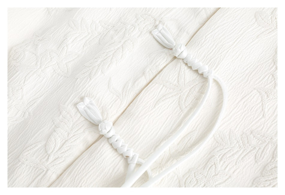 Close-up of white braided drawstring ends on white fabric with a raised floral pattern.