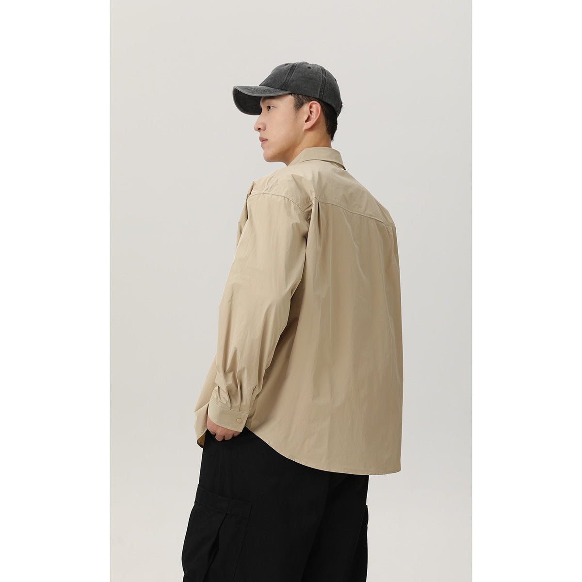 Model shown from behind in a beige shirt with a curved hem and loose black cargo pants.