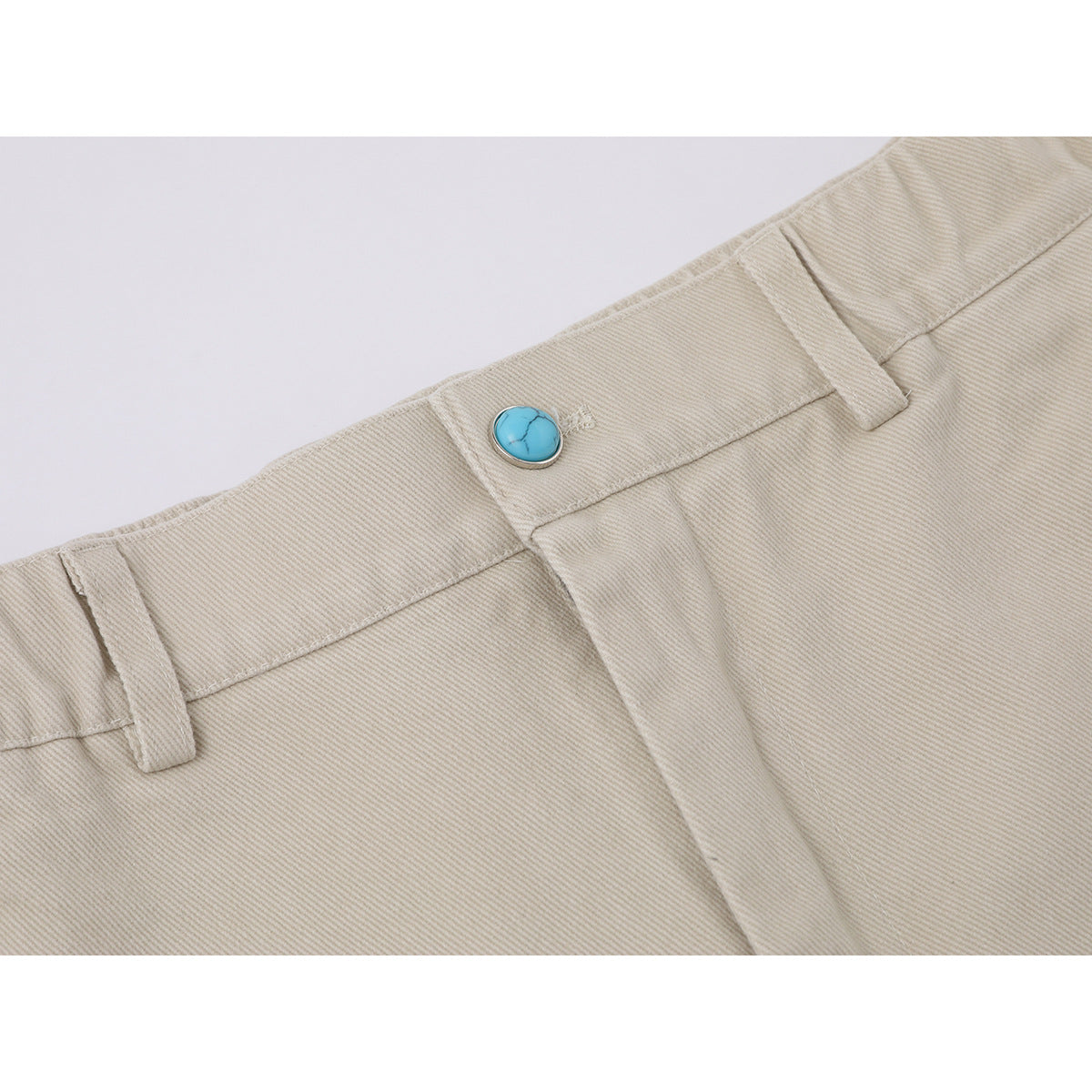Close-up of beige wide-leg trousers showing the waistband, belt loops, fly seam, and turquoise button.