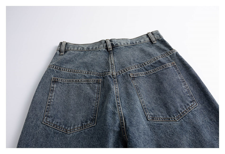 Back view of blue-gray jeans laid flat, showing the waistband, belt loops, center seam, and two patch pockets.