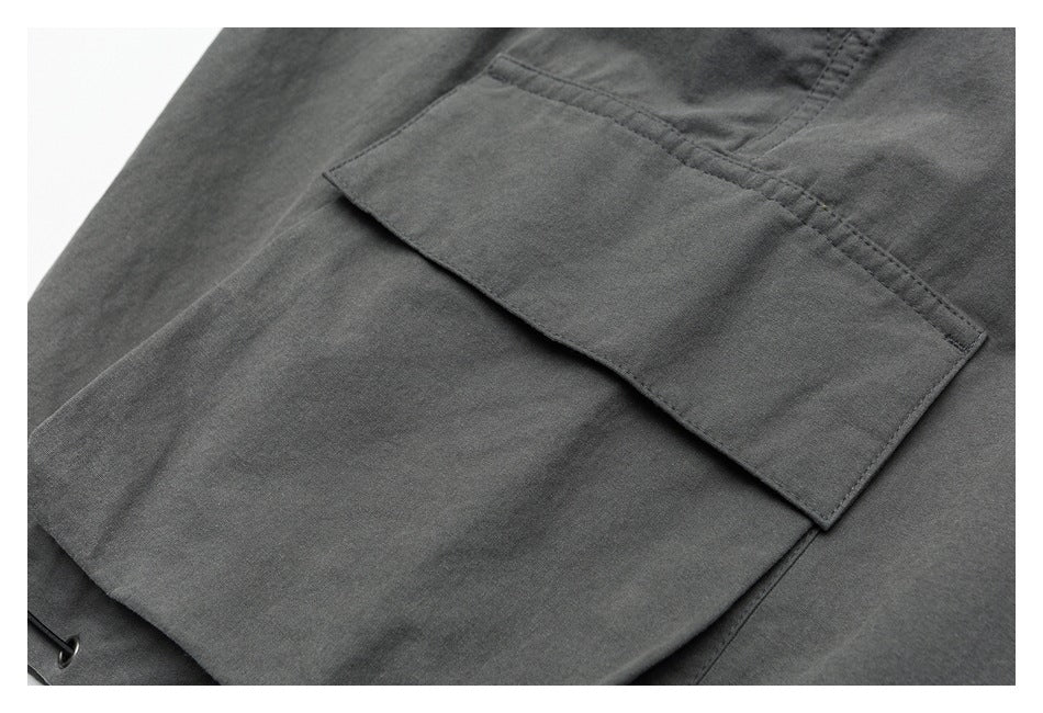 Close-up of a flap pocket on charcoal-gray trousers, with visible stitching and a small metal eyelet nearby.