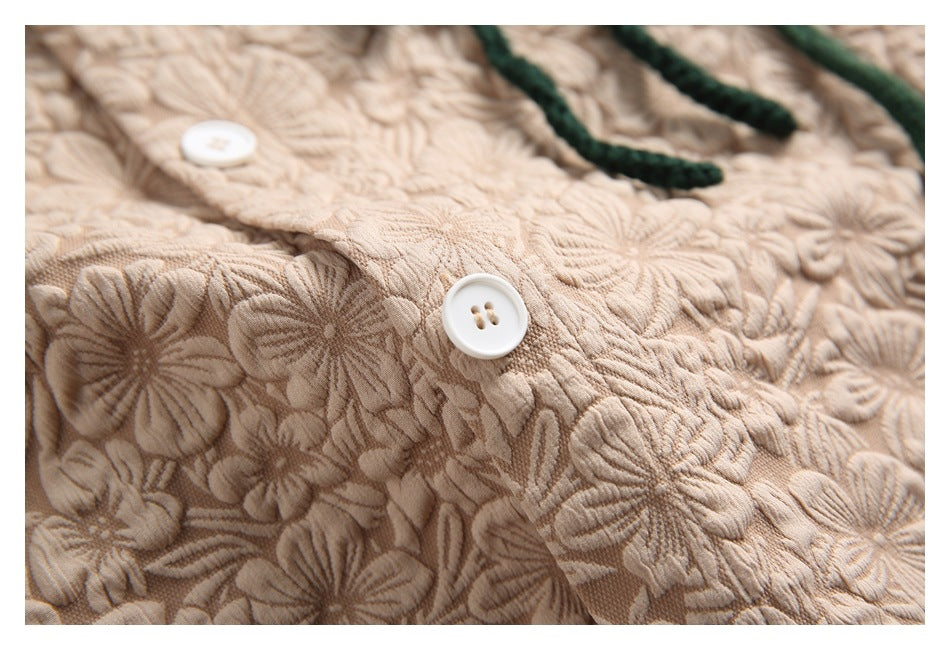 Close-up of a white button against the shirt's raised beige floral pattern.