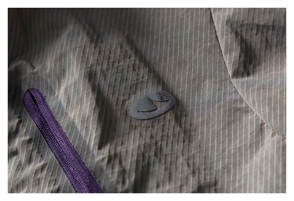 Close-up of a dark emblem and purple zipper on the gray vest's pinstriped fabric.
