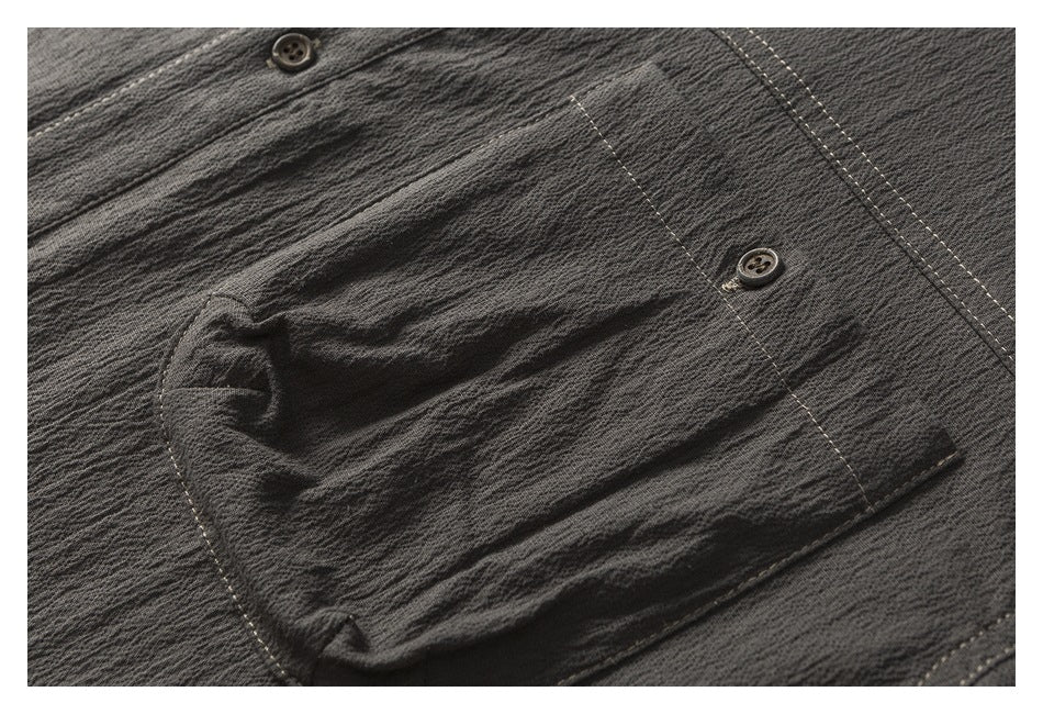 Close-up of the charcoal shirt's chest pocket, dark button, textured surface, and contrast stitching.