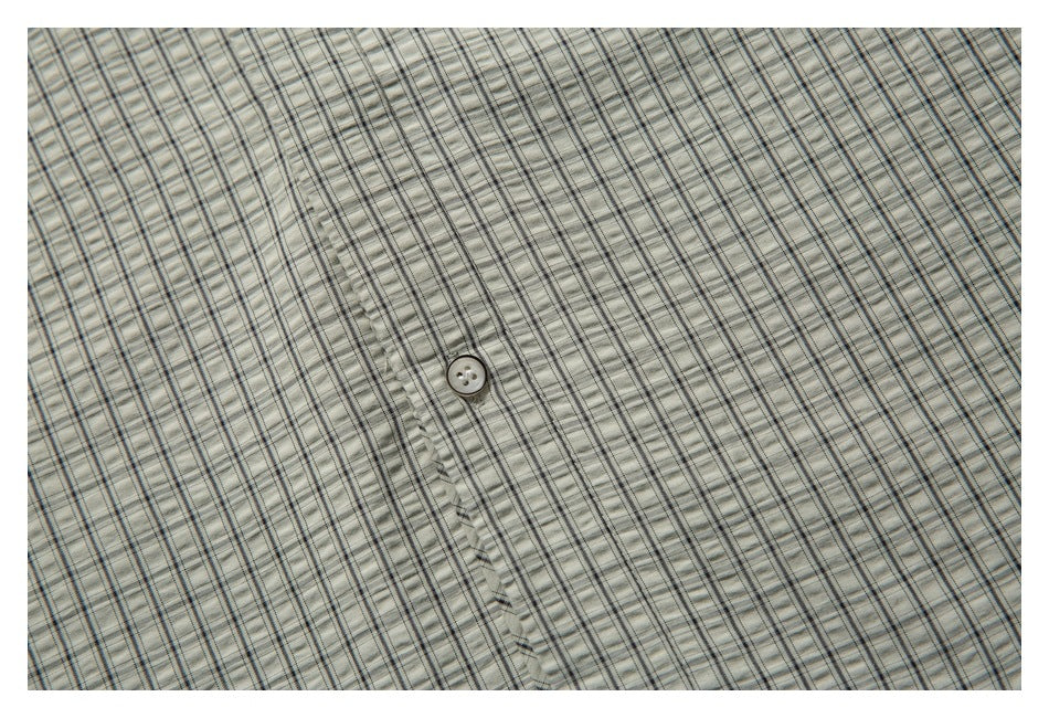 Close-up of the shirt's small gray check pattern, button, and stitched placket.