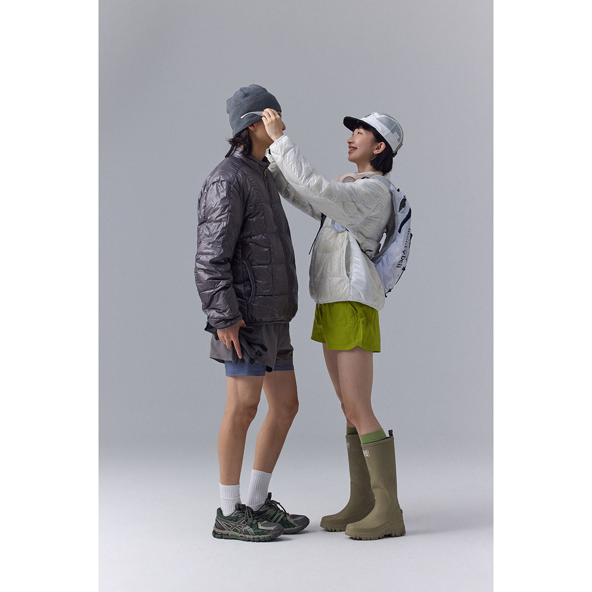 Two models in outdoor outfits; one wears a dark gray quilted jacket and the other a white jacket.