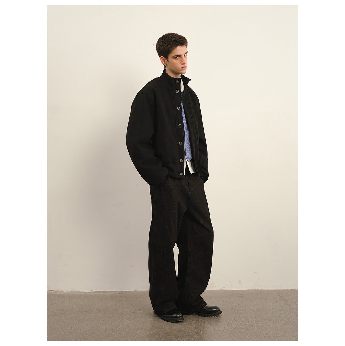 Model wearing a black button-front jacket, blue striped tie and wide-leg black trousers.