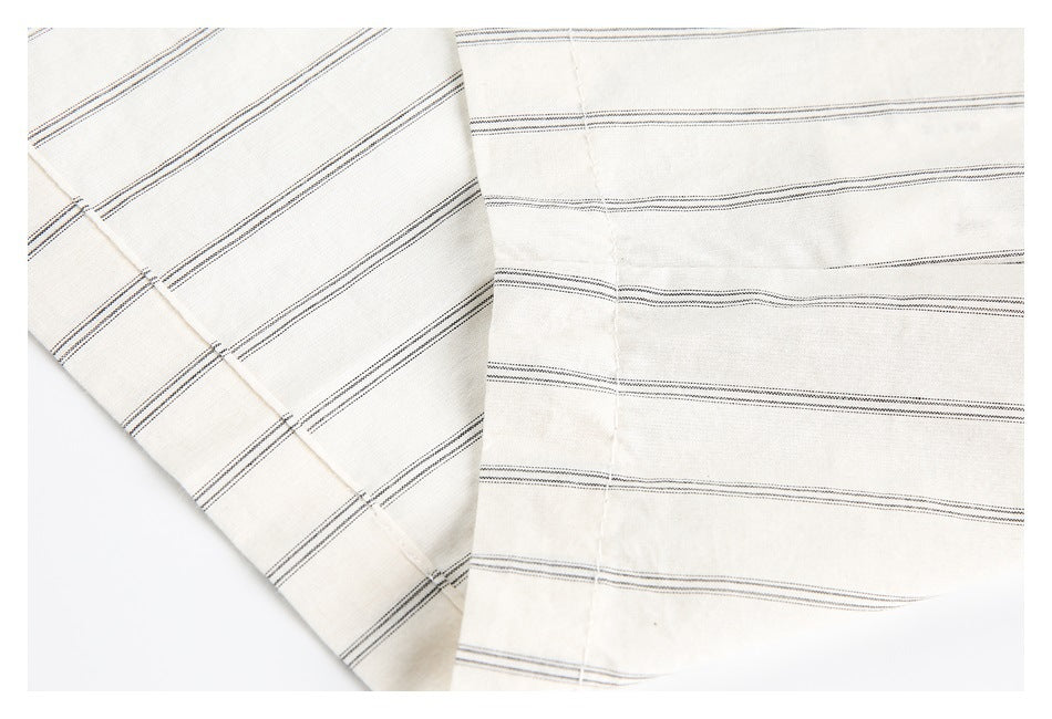 Close-up of off-white fabric with thin dark parallel stripes, folded to show the pattern.