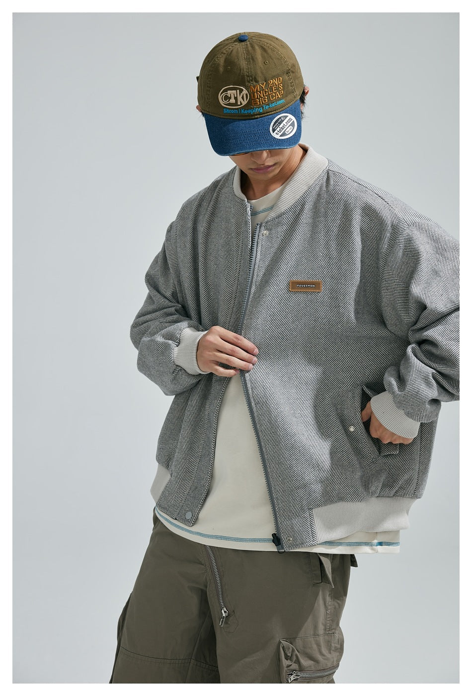Model wearing a gray herringbone zip jacket with white ribbed trim, shown from the front.