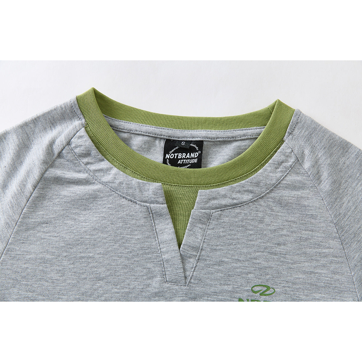 Close-up of a gray long-sleeve top with a green ribbed neckline and split V-notch; inner brand label visible.