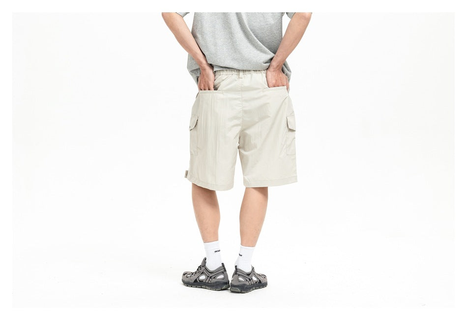 Cropped view of a model wearing cream cargo shorts, a gray T-shirt, white socks, and gray sandals; front view.
