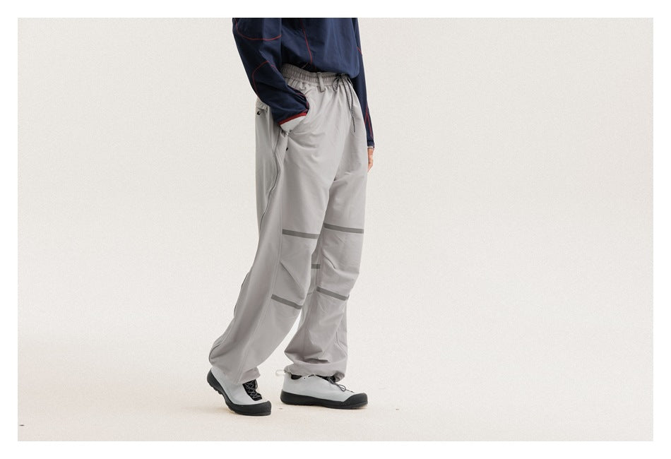 Side-front view of a cropped model wearing loose light-gray drawstring pants with dark bands across the legs.