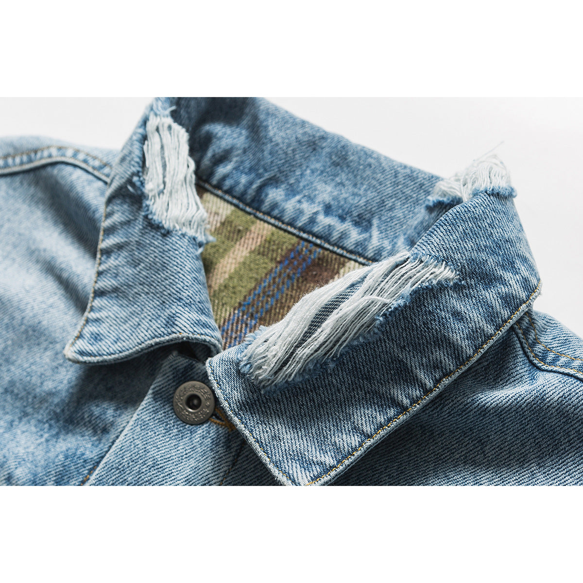 Close-up of a light blue denim jacket collar with frayed edges and a glimpse of plaid lining.