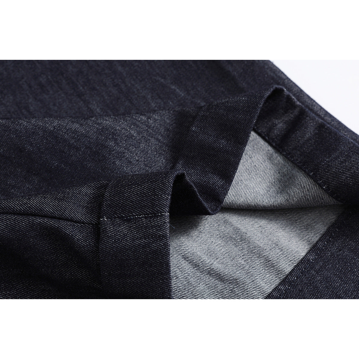 Close-up of dark indigo fabric folded to show its lighter reverse side and stitched edge.