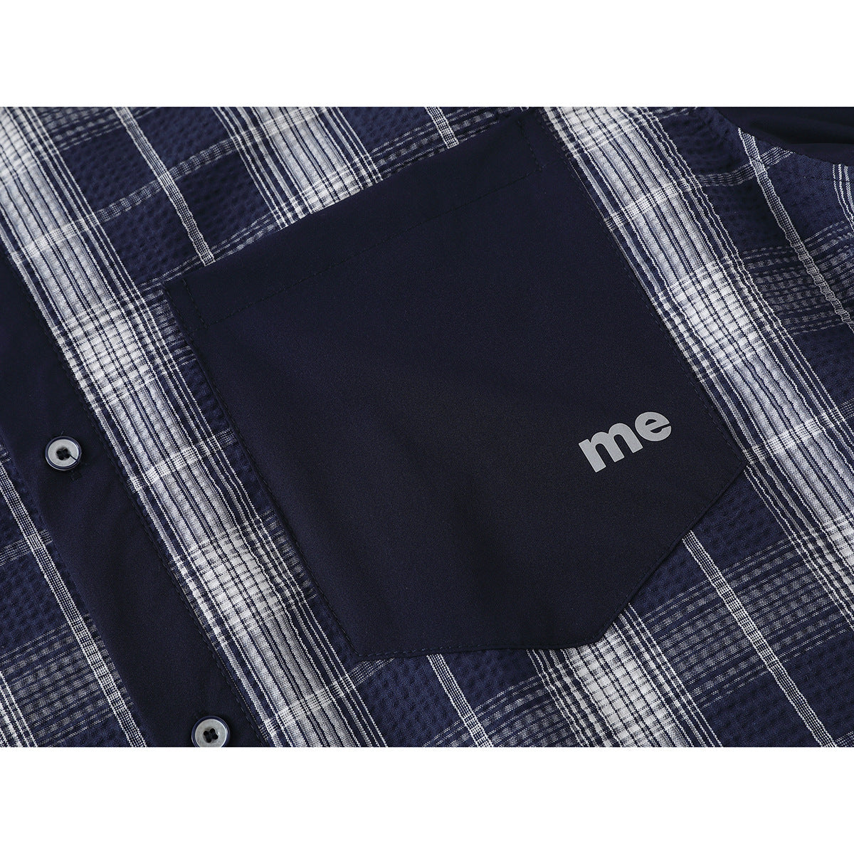 Close-up of a navy pocket with small white “me” lettering on a blue-and-white plaid shirt.