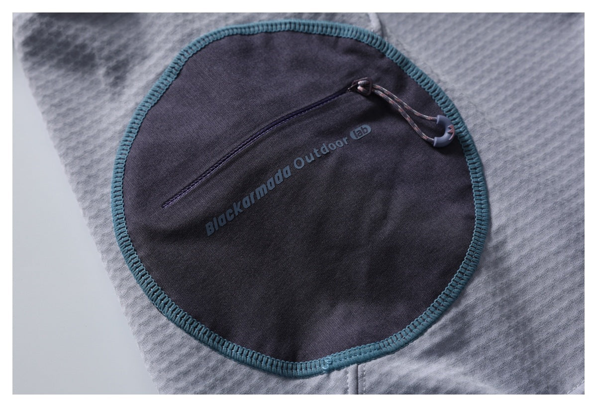 Close-up of a dark gray garment pocket with teal overlock edging, a diagonal zip, and English text printed on the pocket.