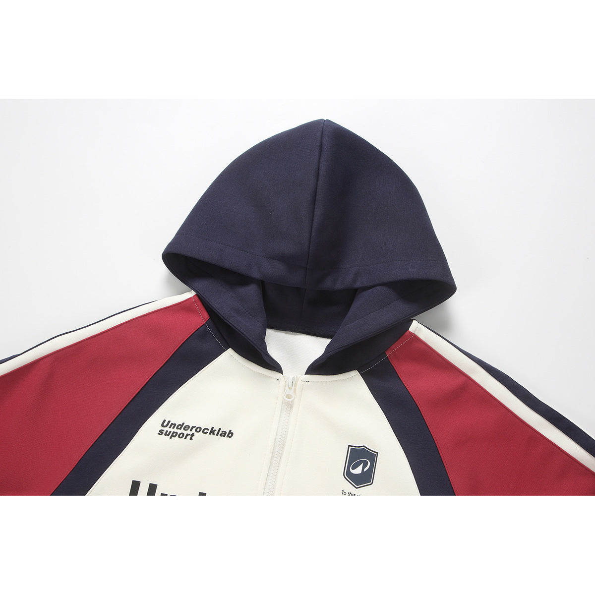 Close view of a cream zip-up hoodie with a navy hood and red and navy color-block sleeves.