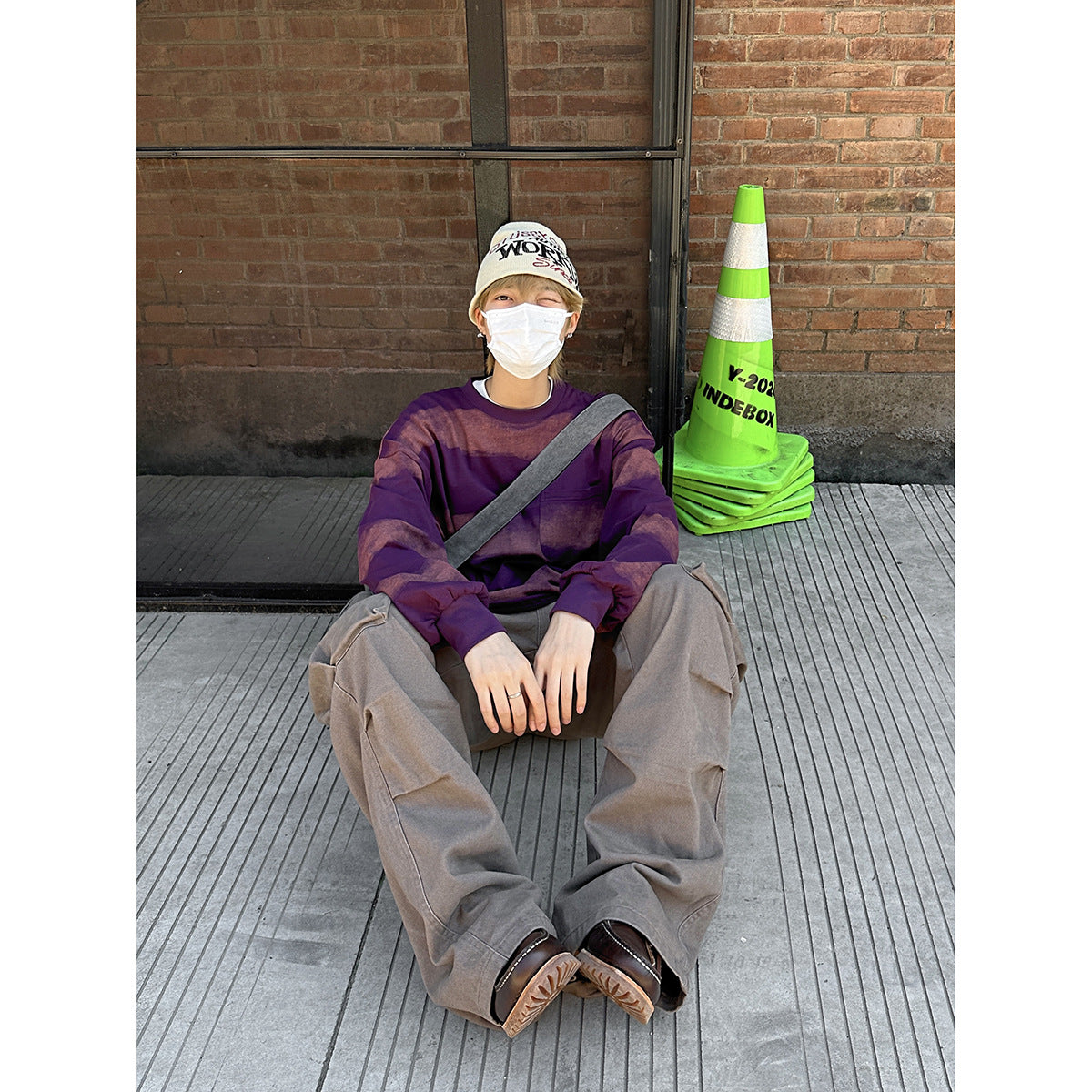 Seated model wearing a loose purple sweatshirt with broad muted rose stripes and a chest pocket.