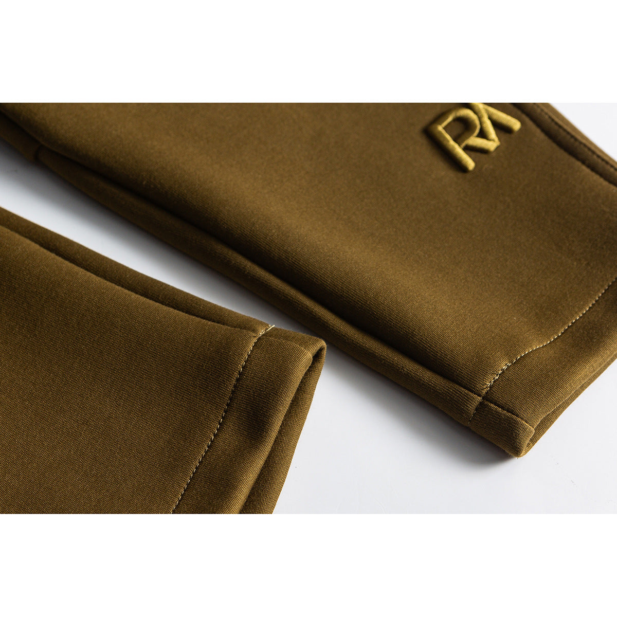 Close-up of mustard pants showing a small embroidered emblem and stitched hem.