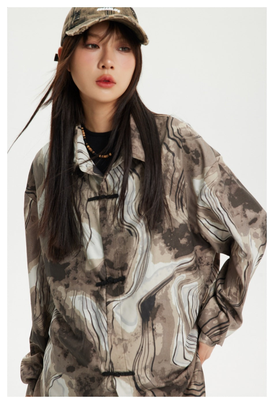 Close front view of a model in a brown, taupe, and ivory abstract-print shirt with black frog closures.