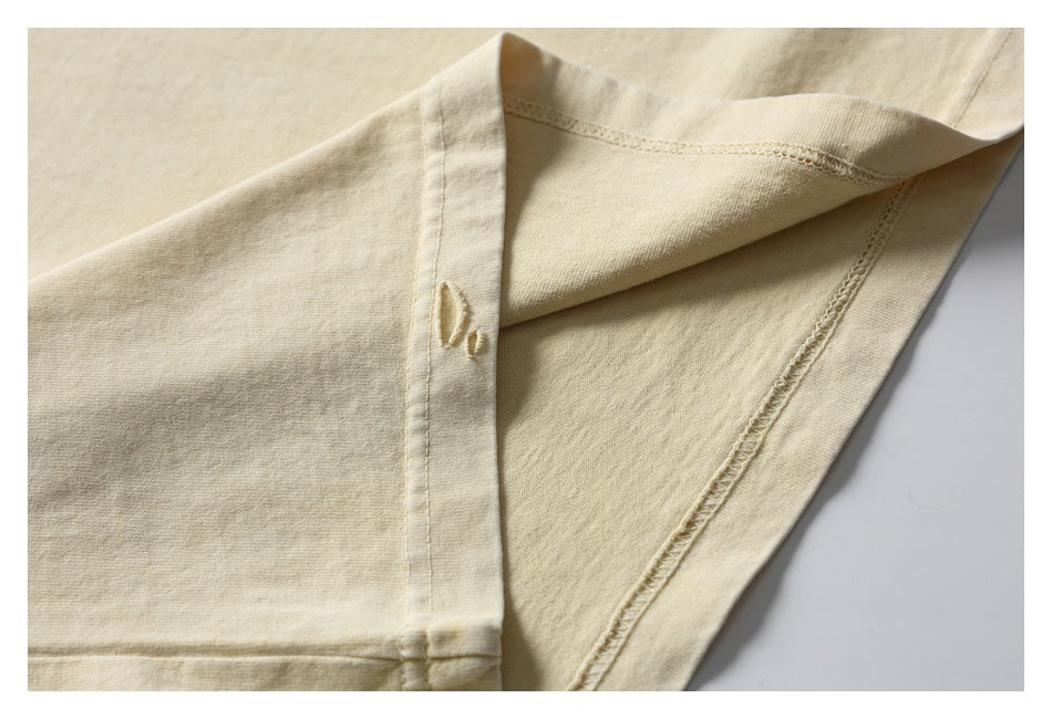 Close-up of the pale cream T-shirt’s inside seams and stitching, with a small distressed opening near the sleeve edge.