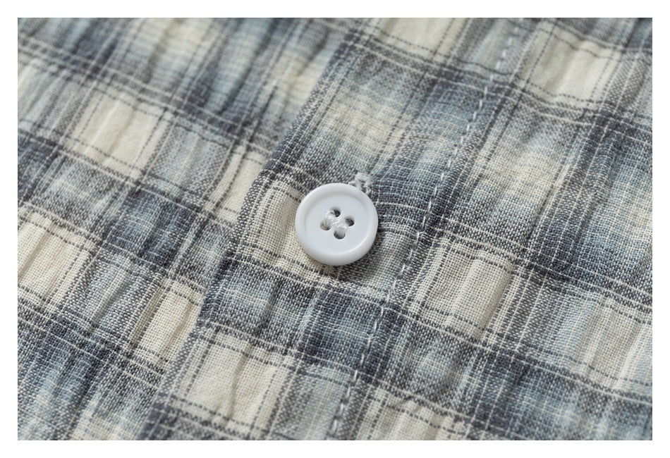 Close-up of a white button on gray, blue, and cream plaid shirt fabric.